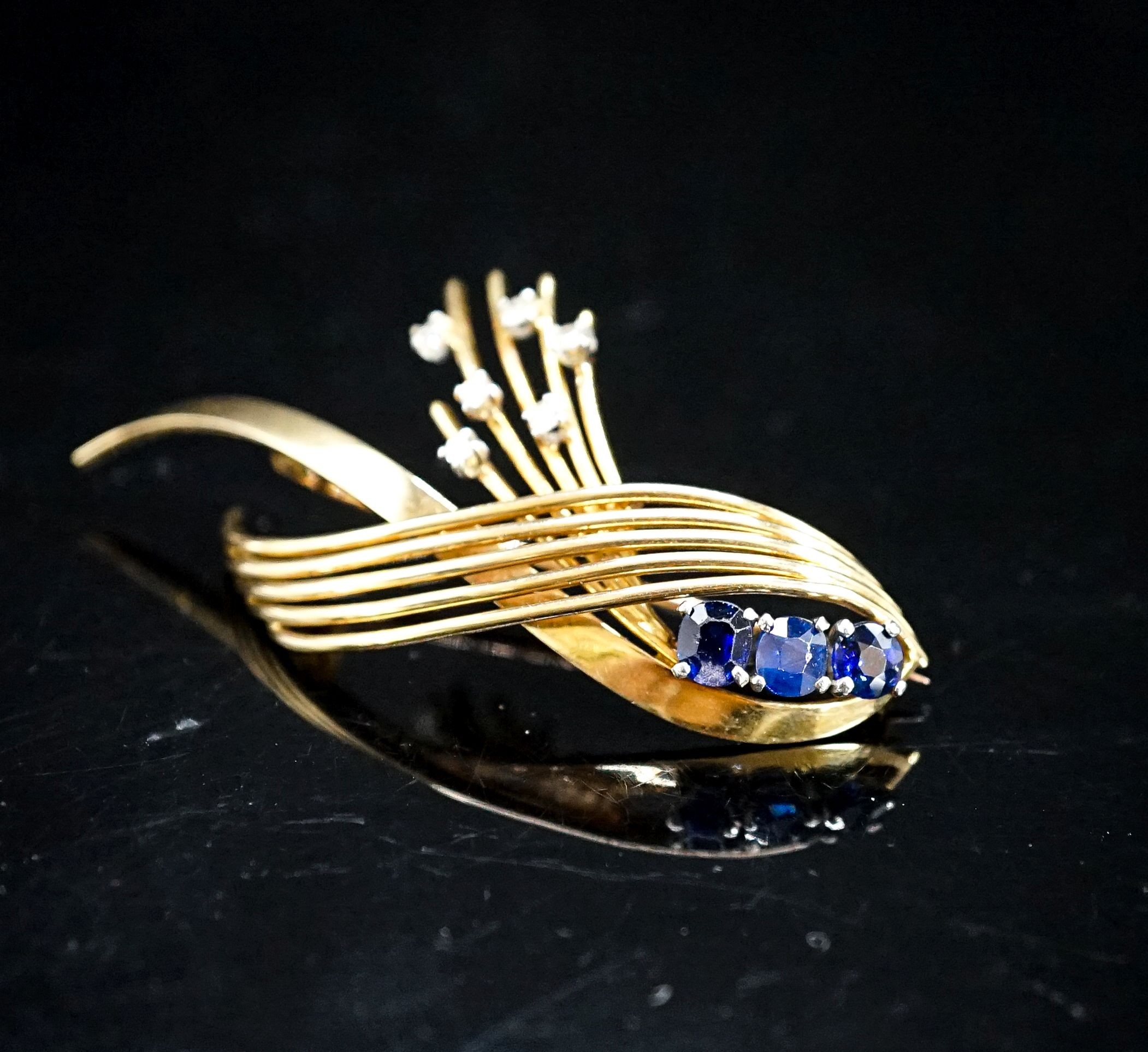 A modern yellow metal, sapphire and diamond set stylised spray brooch, 53mm, gross 9.7 grams.